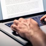 A man's hands types a document on a laptop keyboard.