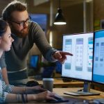 A UX designer consults with her colleague as they review an app design mockup on her computer.