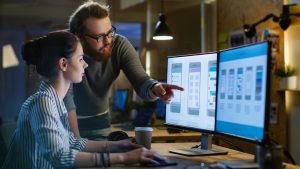 A UX designer consults with her colleague as they review an app design mockup on her computer.