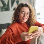 A smiling young woman looks at her phone.