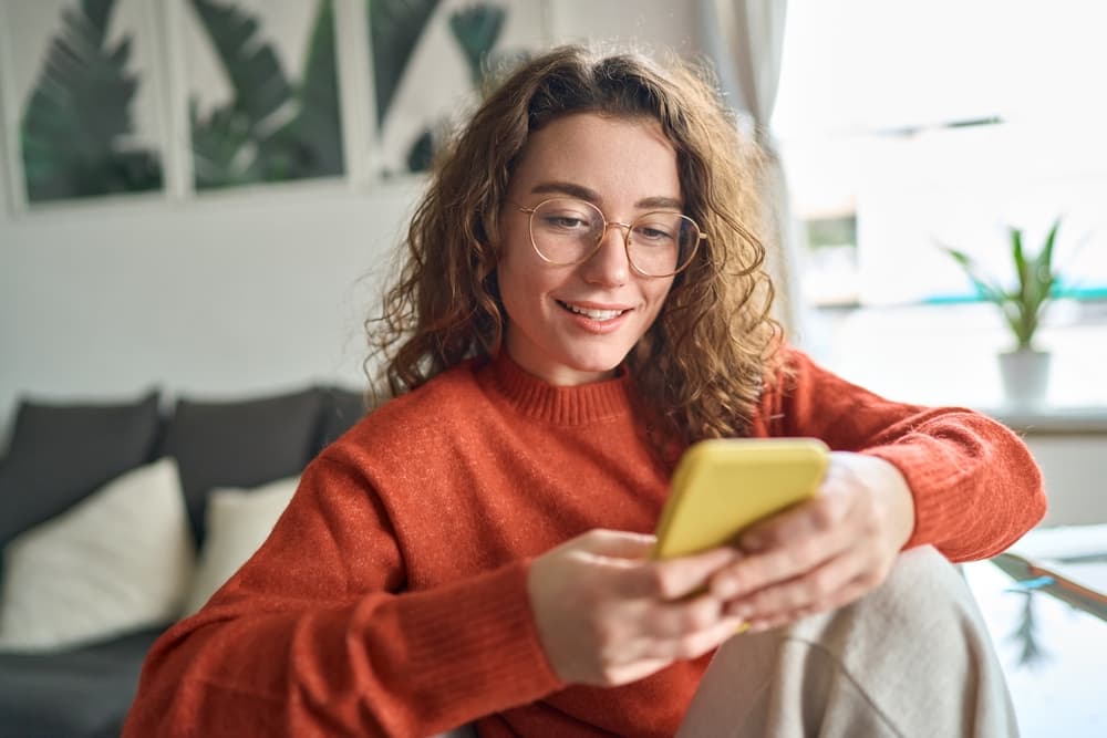 A smiling young woman looks at her phone.