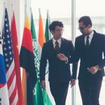 Two negotiators discuss an important issue while walking past a row of international flags.