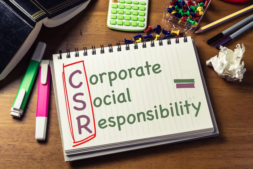 A close-up image of a desk with various work items and a notebook with the words Corporate Social Responsibility in the center.