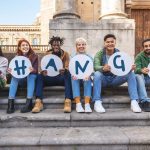 A diverse group of college students sitting outside, each holding a single letter sign that together spells the word “change.”