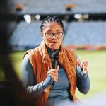 A female sports reporter stands facing the camera as she conducts a post-event wrap-up for her audience.