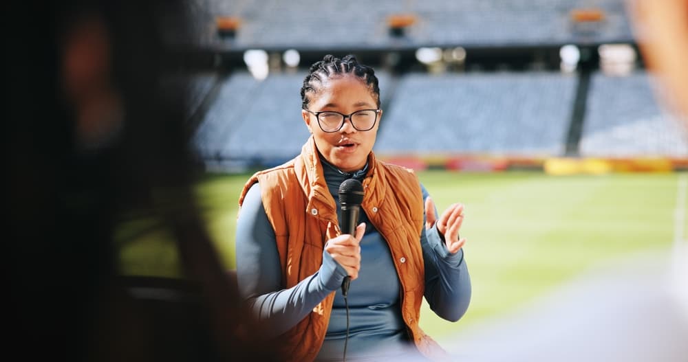 A female sports reporter stands facing the camera as she conducts a post-event wrap-up for her audience.