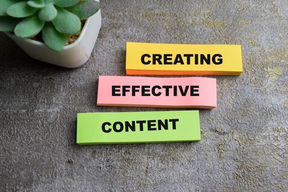 Three colored blocks with the words “creating effective content” sitting on a table with a potted plant in the background.